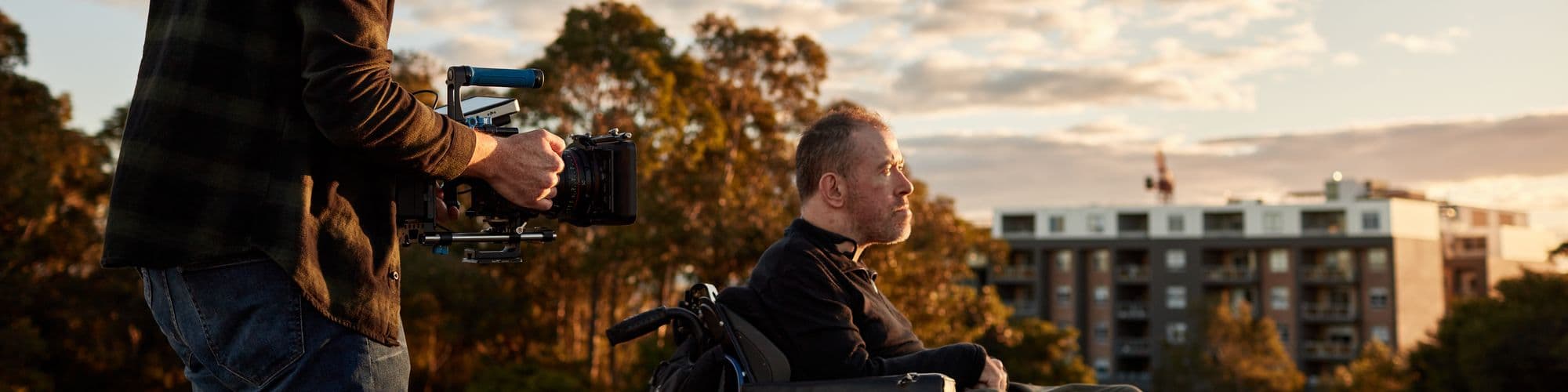 A man using a wheelchair being filmed outdoors.